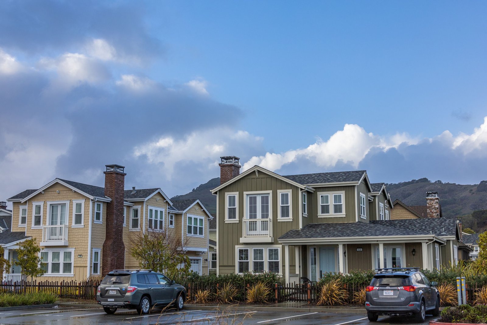 Picturesque suburban neighborhood with modern houses and parked cars under a partly cloudy sky.